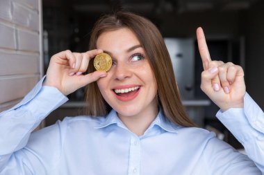 Elinde altın bitcoin kripto para tutan kadın bir fikir ya da soruyla şaşkın şaşkın gülüyor..