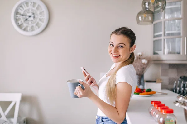 Jovem Mulher Lendo Notícias Engraçadas Telefone Cozinha Bebendo Uma Xícara — Fotografia de Stock