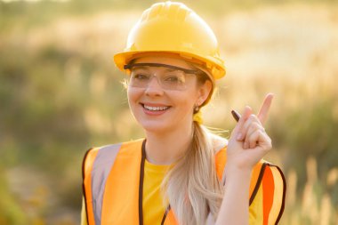 Smiling female worker in protective gear and uniform gestures confidently outdoors during daylight. safety, positivity, and a professional work environment. have idea