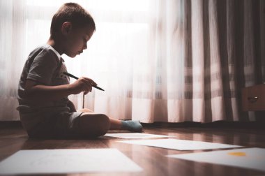 Çocuk ödevini iyi çalışıyor, yazar ve sayfa yere dağılmış kağıt üzerinde çizer