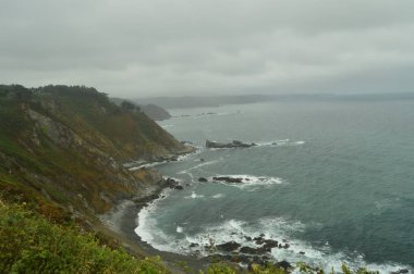 Cliffs Las Llanas Beach onların taşlara karşı yağmurlu bir günde kırma dalgalar deniz ile yeşil. 29 Temmuz 2015. Manzara, Doğa, seyahat. San Esteban De Pravia, Asturias, İspanya.
