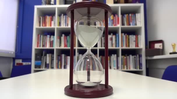 Hourglass in the office on the table on the background of the bookcase — Stock Video