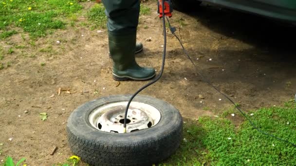 Un hombre infla una rueda vieja del coche con un compresor . — Vídeos de Stock