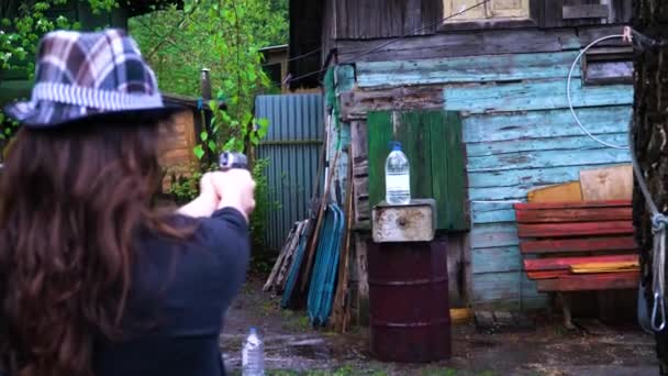 La chica en el sombrero dispara un arma y dispara una botella de agua — Vídeos de Stock