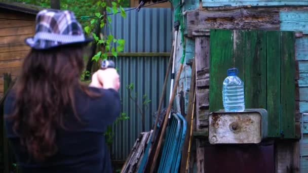Ta holka v klobouku střílí pistolí, kulka střílí lahví vody — Stock video