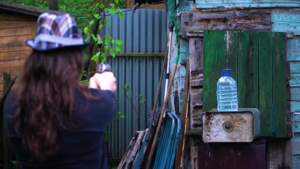 Das Mädchen mit dem Hut schießt mit einer Pistole in eine Wasserflasche — Stockvideo