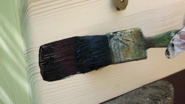 Man schildert het houten oppervlak met zwarte verf — Stockvideo