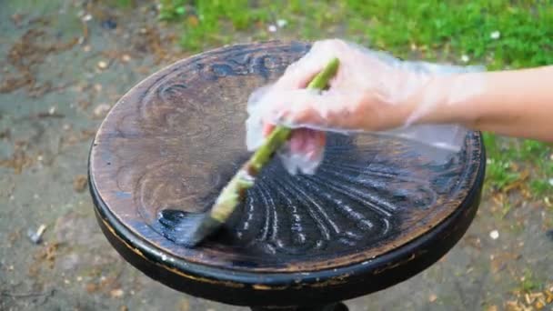 Man puts black paint on the worn surface of the piano chair — Stock Video