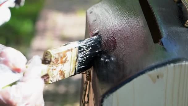 De man schildert zorgvuldig met een borstel met zwarte verf de deksel van de borst — Stockvideo