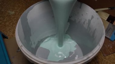 Turkuaz boya beyaz bir plastik kovaya dökülür.
