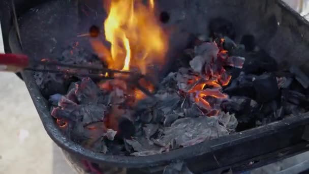 Pieces of paper are smoldering in the barbecue among the coals — ストック動画