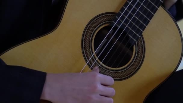 De handen van een jongeman die de snaren van een klassieke gitaar vingert — Stockvideo