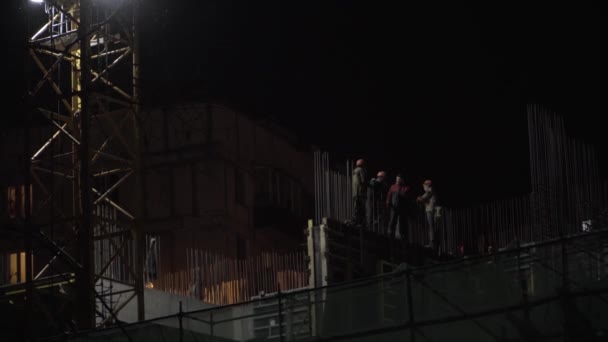 Por la noche en el sitio de construcción un grupo de constructores fuman — Vídeos de Stock