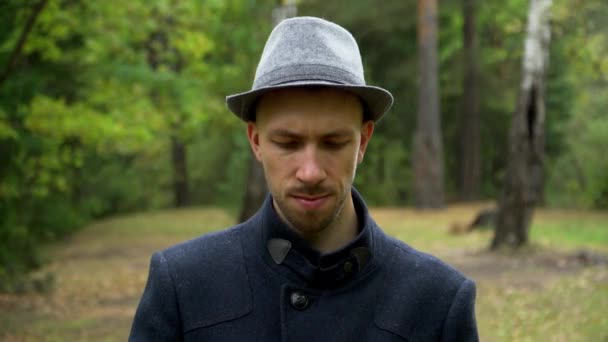 Een man met hoed en jas staat rustig in de regen in het bos — Stockvideo