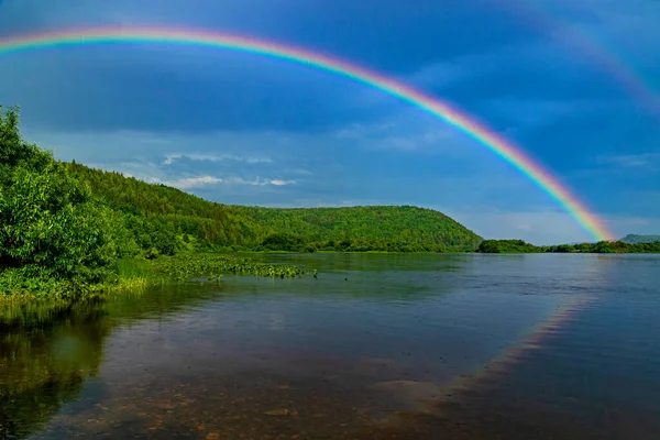 曇った空に対する水の反射と川の上の虹 ストック写真