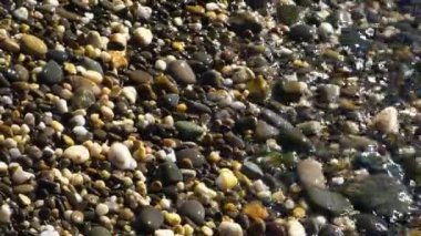 Şeffaf deniz dalgaları kıyıları küçük yuvarlak taşlarla yıkıyor.
