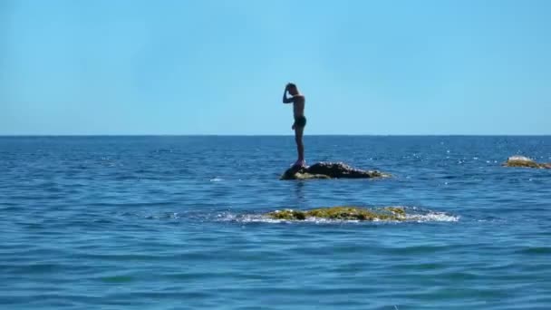 한 스포츠 선수가 바다 한 가운데 바위 위에 서서 물 속으로 뛰어들었습니다 — 비디오