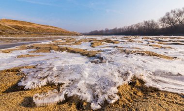 Soğuk bir kış sabahı, vahşi bir nehir kıyısında, kar ve donla