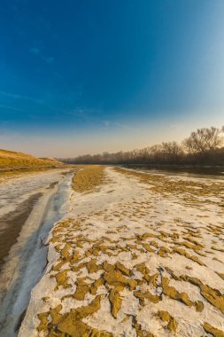 Soğuk bir kış sabahı, vahşi bir nehir kıyısında, kar ve donla