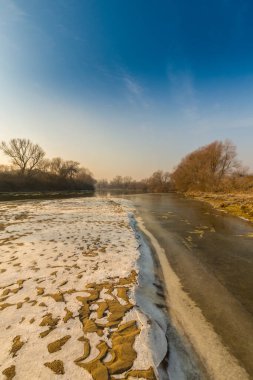 Soğuk bir kış sabahı, vahşi bir nehir kıyısında, kar ve donla