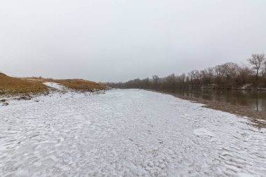 Vahşi bir nehir kıyısındaki soyut kum tepecikleri, taze kar tozuyla kaplı.