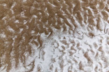 Vahşi bir nehir kıyısındaki soyut kum tepecikleri, taze kar tozuyla kaplı.