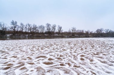 Vahşi bir nehir kıyısındaki soyut kum tepecikleri, taze kar tozuyla kaplı.