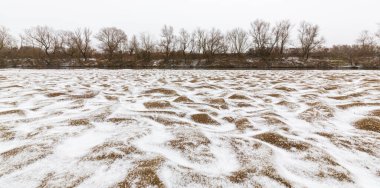 Vahşi bir nehir kıyısındaki soyut kum tepecikleri, taze kar tozuyla kaplı.