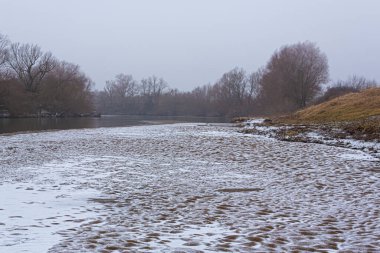 Vahşi bir nehir kıyısındaki soyut kum tepecikleri, taze kar tozuyla kaplı.