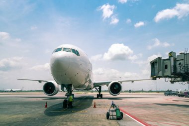 Uluslararası havaalanının terminal kapısında, bulutlu mavi gökyüzü arka planında, modern yolcu veya kargo uçağı otoparkında teknisyen ya da mühendis kontrolü