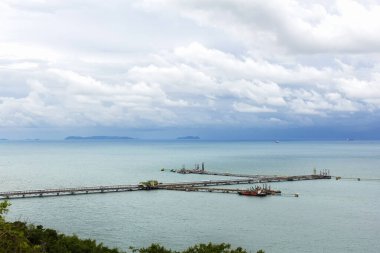 Chonburi Tayland 'daki alacakaranlık bulutlarının altında denizden ithalat için çalışan vinçle liman ve köprü manzarası çok güzel.