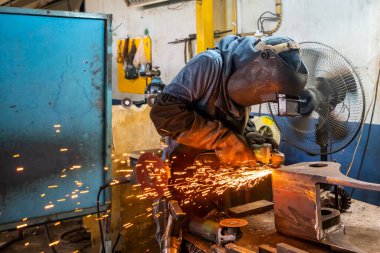 İnsan ya da işçi fabrikadaki elektrikli tekerlek öğütme makinesinin kaynak parçalarını cilalıyor.