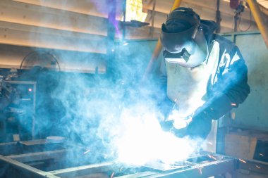 İnsan ya da işçi fabrikada metal parçalarını çok duman ve parlaklıkla kaynatıyorlar.