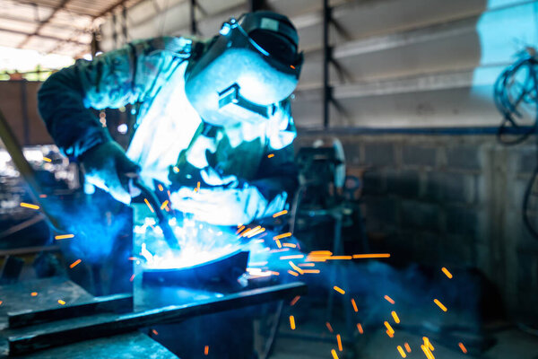 man or worker welding metal part at factory with very smoke and sparkle bright right blur background