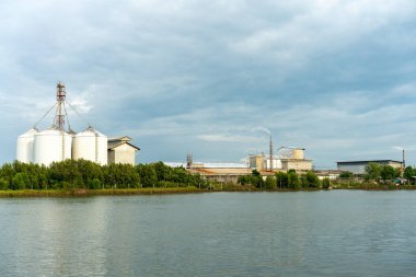 Akşamları deniz kıyısında bulutlu gökyüzü olan büyük sanayi ve silo binaları.