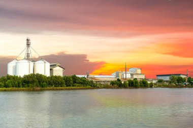 Akşamları deniz kıyısında büyük bir sanayi fabrikası ve silo inşaatı. Gün batımında güzel, altın, sarı ve kızıl gökyüzü.