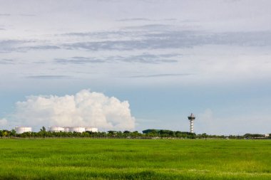 Hava trafik yönetimi için havaalanı kontrol kulesi. Hava bulutlu arka planda, petrol tankının yanındaki yeşil alanda.
