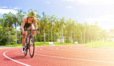 Asyalı genç bayan sporcular yarış pistinde bisiklet sürüyorlar. Açık hava spor sahasında güneş ışığıyla.