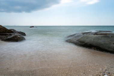 Tayland 'da öğleden sonra bulutlu güzel deniz ve mavi gökyüzü ile sahilde kayalar (uzun pozlama))