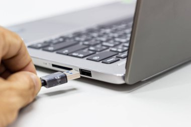 Ofiste beyaz masada dizüstü bilgisayara bağlı bir Usb aygıtı tutan bir iş adamın elini.