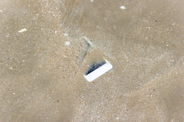 Biały telefon komórkowy pływał do morza na plaży. — Zdjęcie stockowe