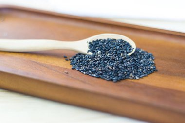 Tahta kaşıkta siyah susam tohumları ahşap masada yığılıyor. 