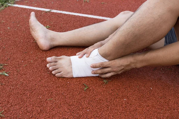 man applying compression bandage onto ankle injury of a football player, Sports injuries, concept First aid for ankle injuries