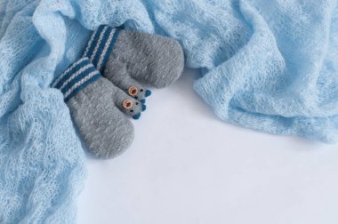 Mavi yün kumaş tarafından çevrili beyaz bir arka planda gri örgü eldiven çifti.