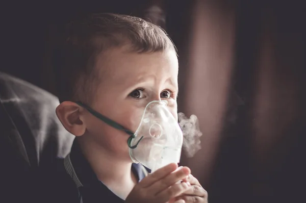 Two year old boy making inhalation with nebulizer at home.