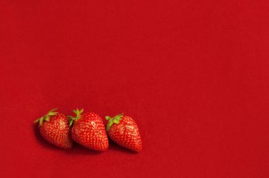 Kırmızı tekstil arka planda üç taze çilek