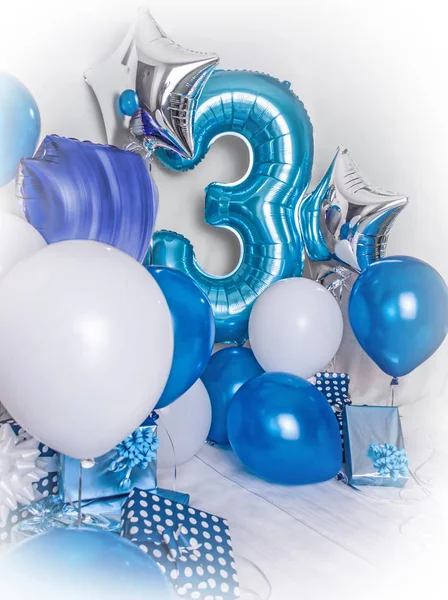 Room decorated for a birthday party with blue, white and silver baloons, presents boxes and ribbons.