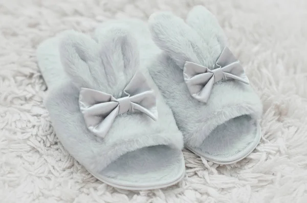 Beautiful fur slippers in a shape of a rabbit on a white furry carpet.