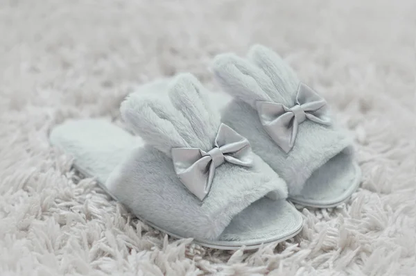 Beautiful fur slippers in a shape of a rabbit on a white furry carpet.