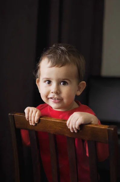 Mignon garçon de 2 ans dans une chemise rouge posant debout sur une chaise . — Photo